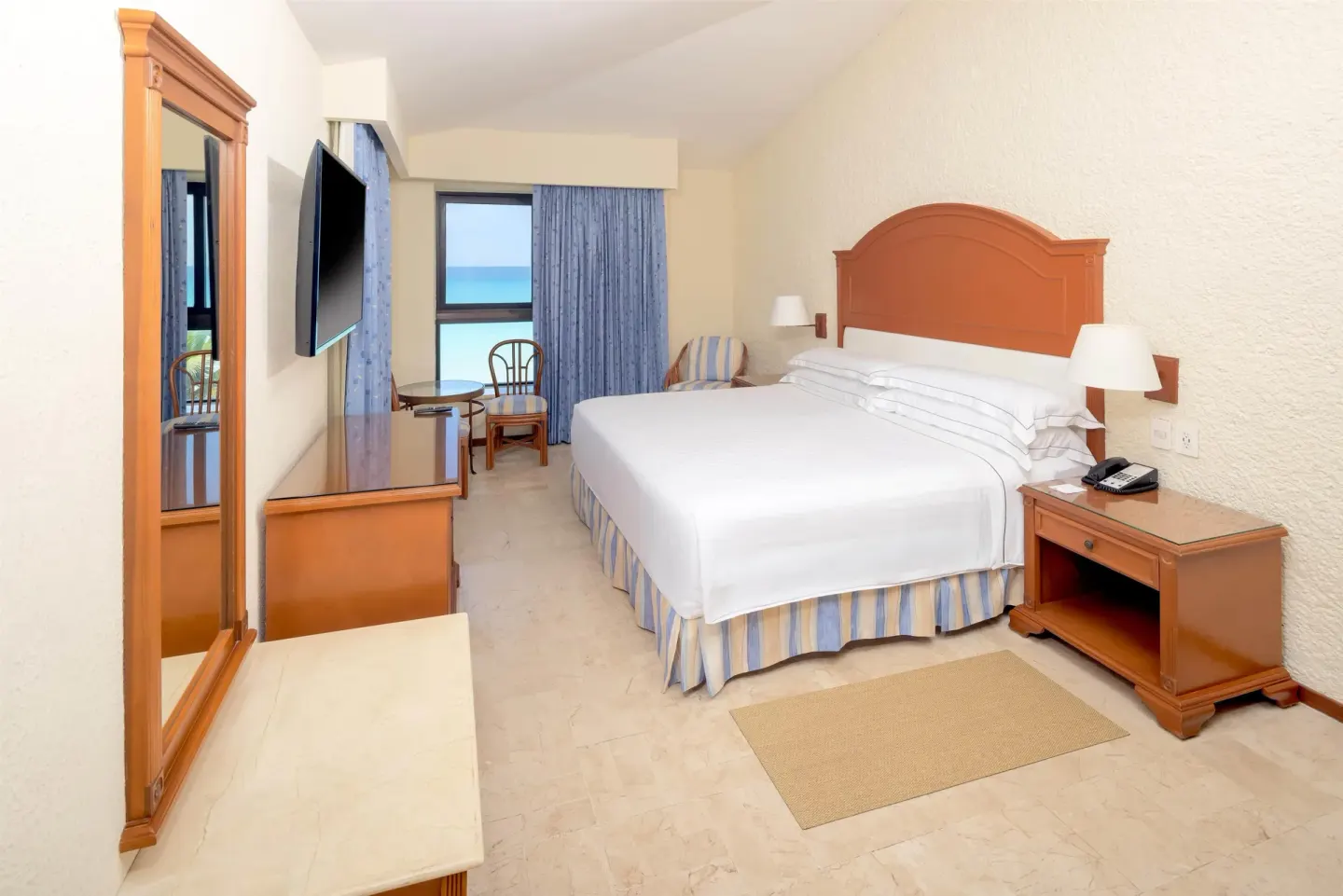 King guest room with dresser, wall TV and ocean-facing window at Occidental Tucancún.