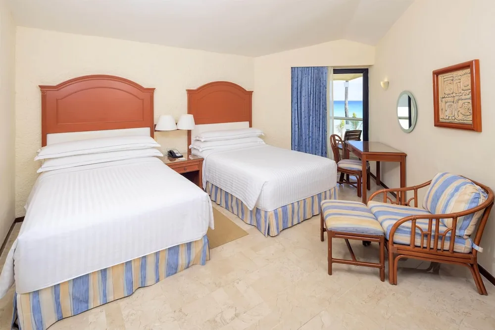 Two-bed guest room with sitting chair and partial ocean view at Occidental Tucancún.