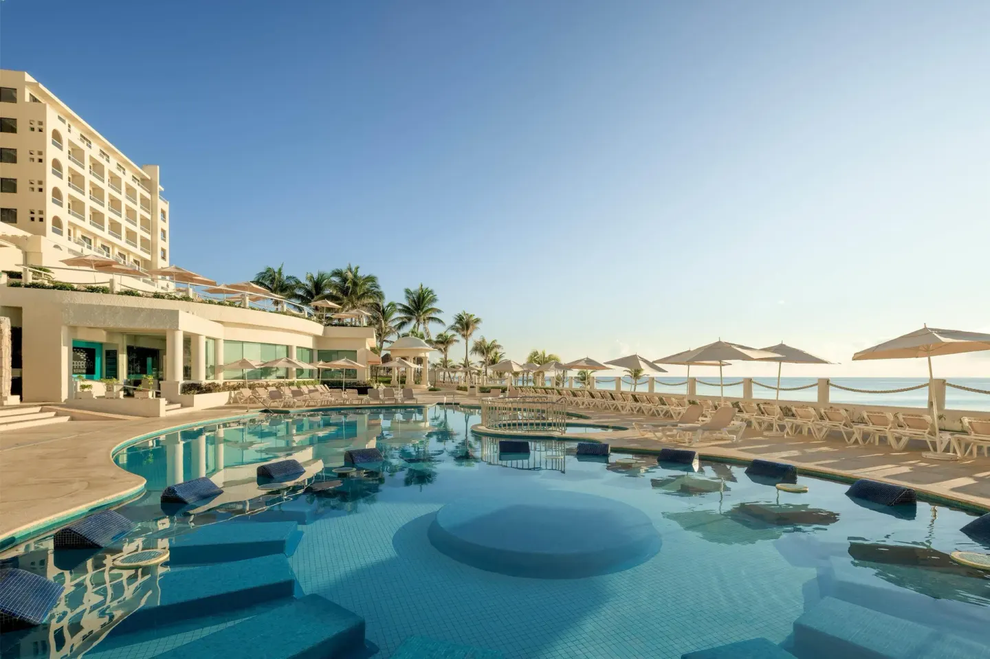 Oceanfront pool with loungers, umbrellas, and resort building at Occidental Tucancún.