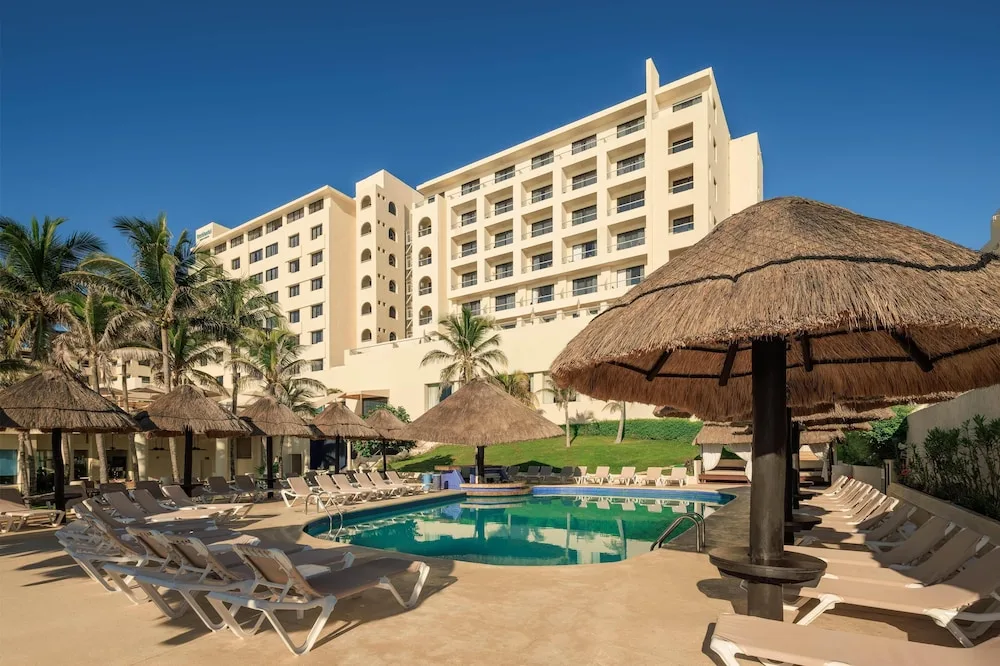 Pool deck with lounge chairs, palapa umbrellas, and hotel building at Occidental Tucancún.