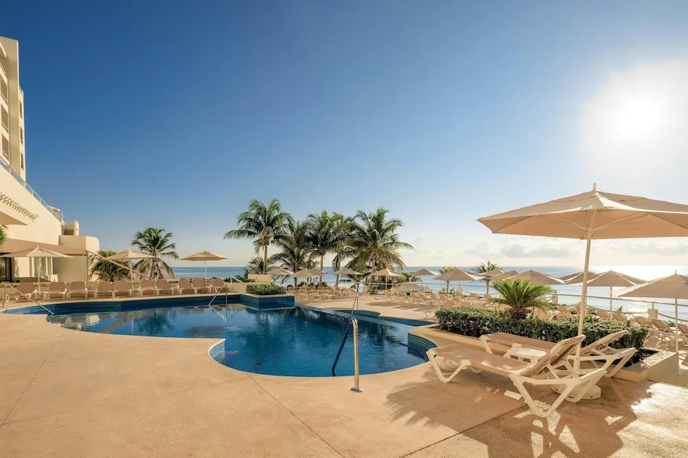 Pool terrace with umbrellas, loungers, palms, and ocean view at Occidental Tucancún.