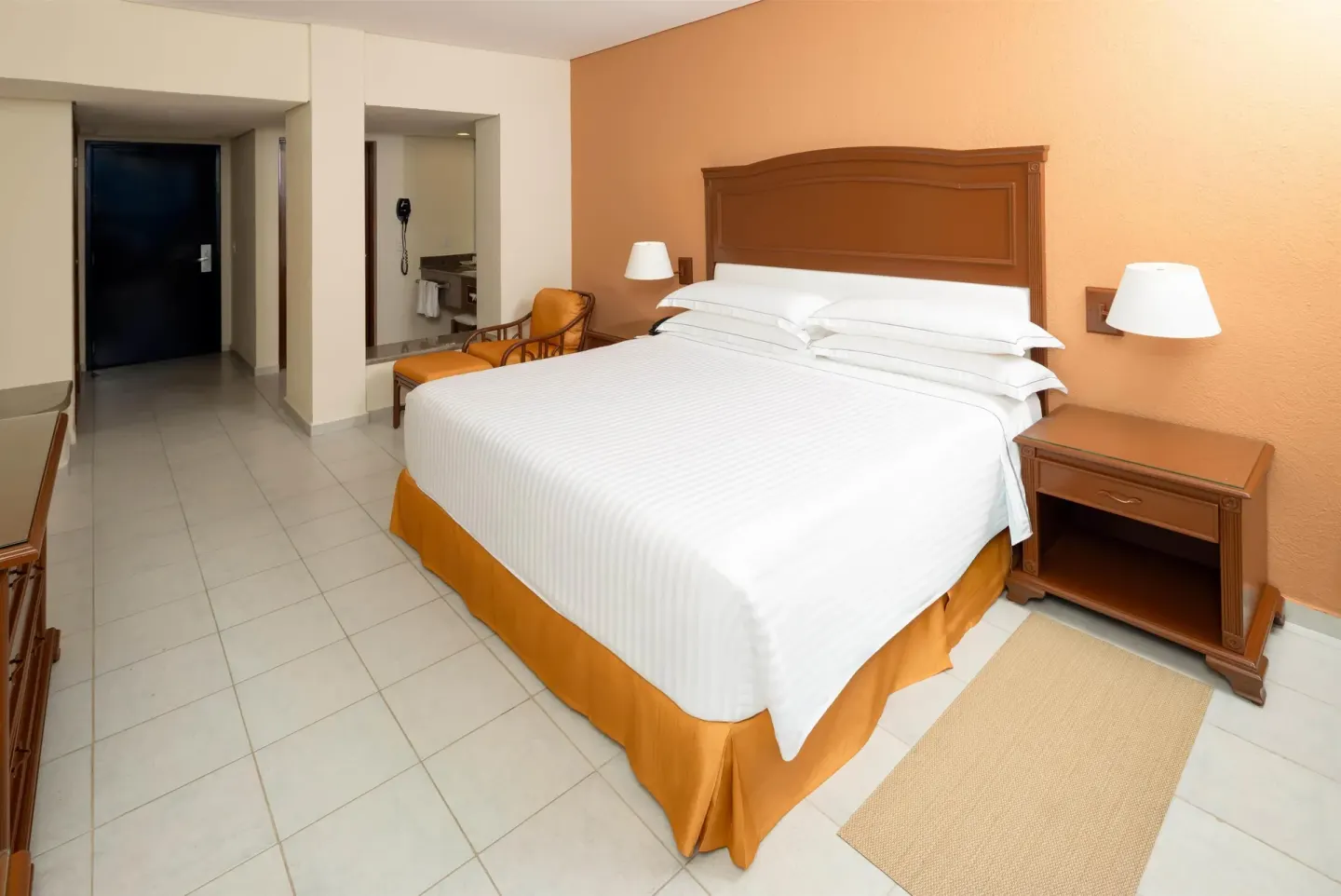 King bed guest room with nightstands and open vanity area at Occidental Tucancún.