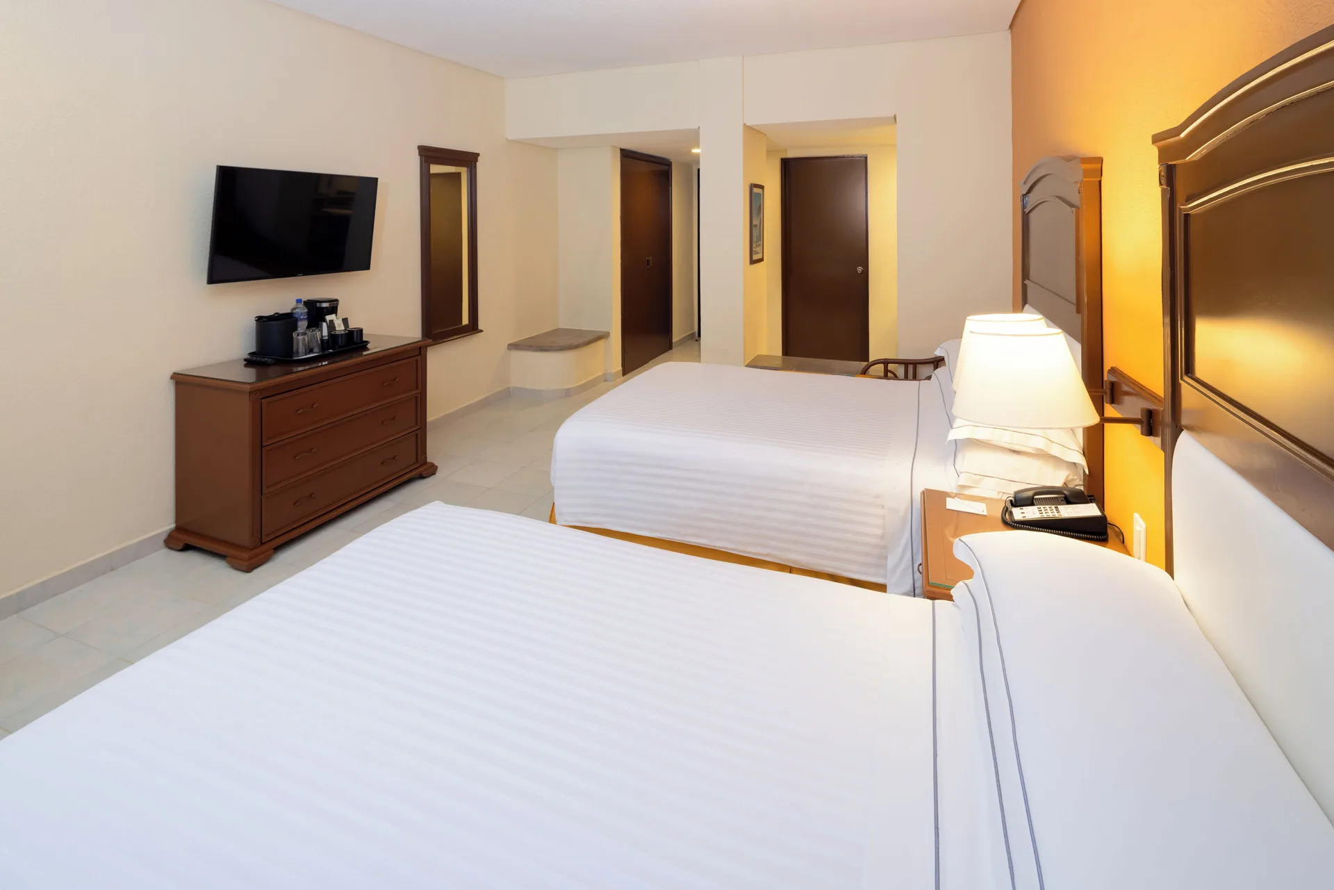 Two-bed guest room with dresser and wall TV at Occidental Tucancún.