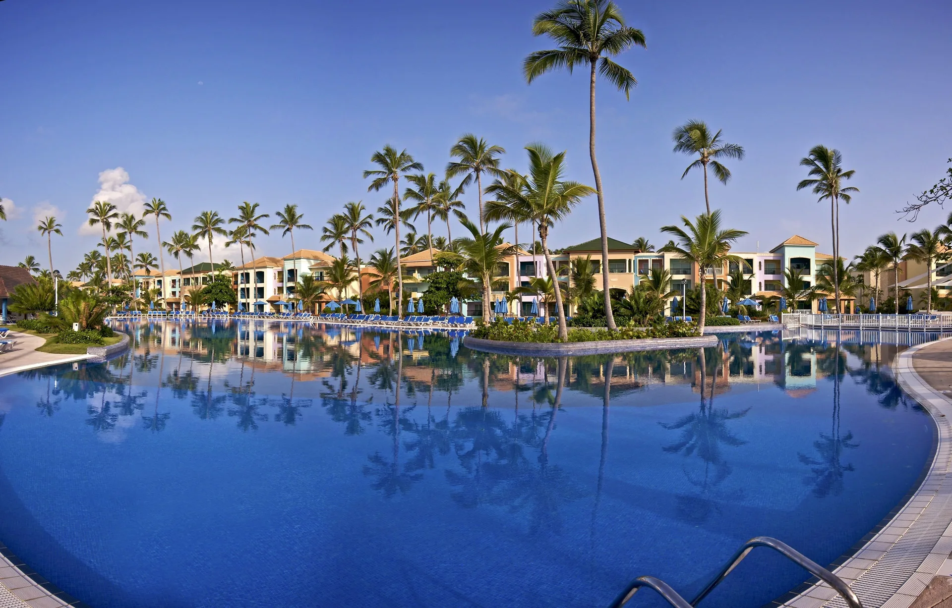 Broad pool with steps, palms and guest buildings at Ocean Blue & Sand Beach Resort.