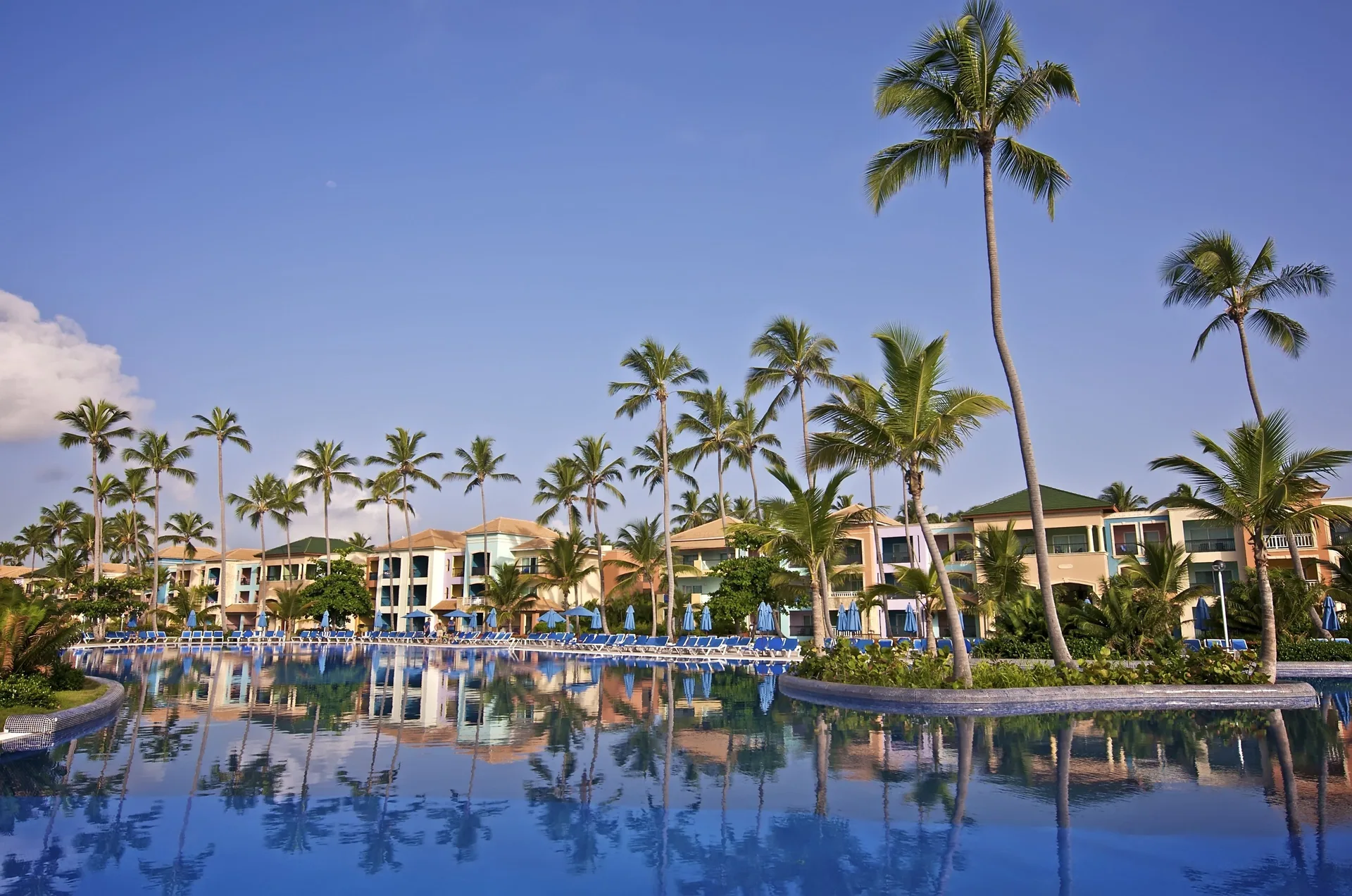 Curving pool bordered by palms, blue loungers and resort buildings at Ocean Blue & Sand Beach Resort.