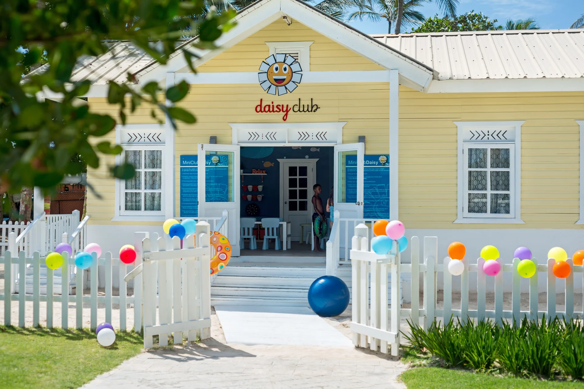 Yellow kids club building with a white fence and colorful balloons at Ocean Blue & Sand Beach Resort.