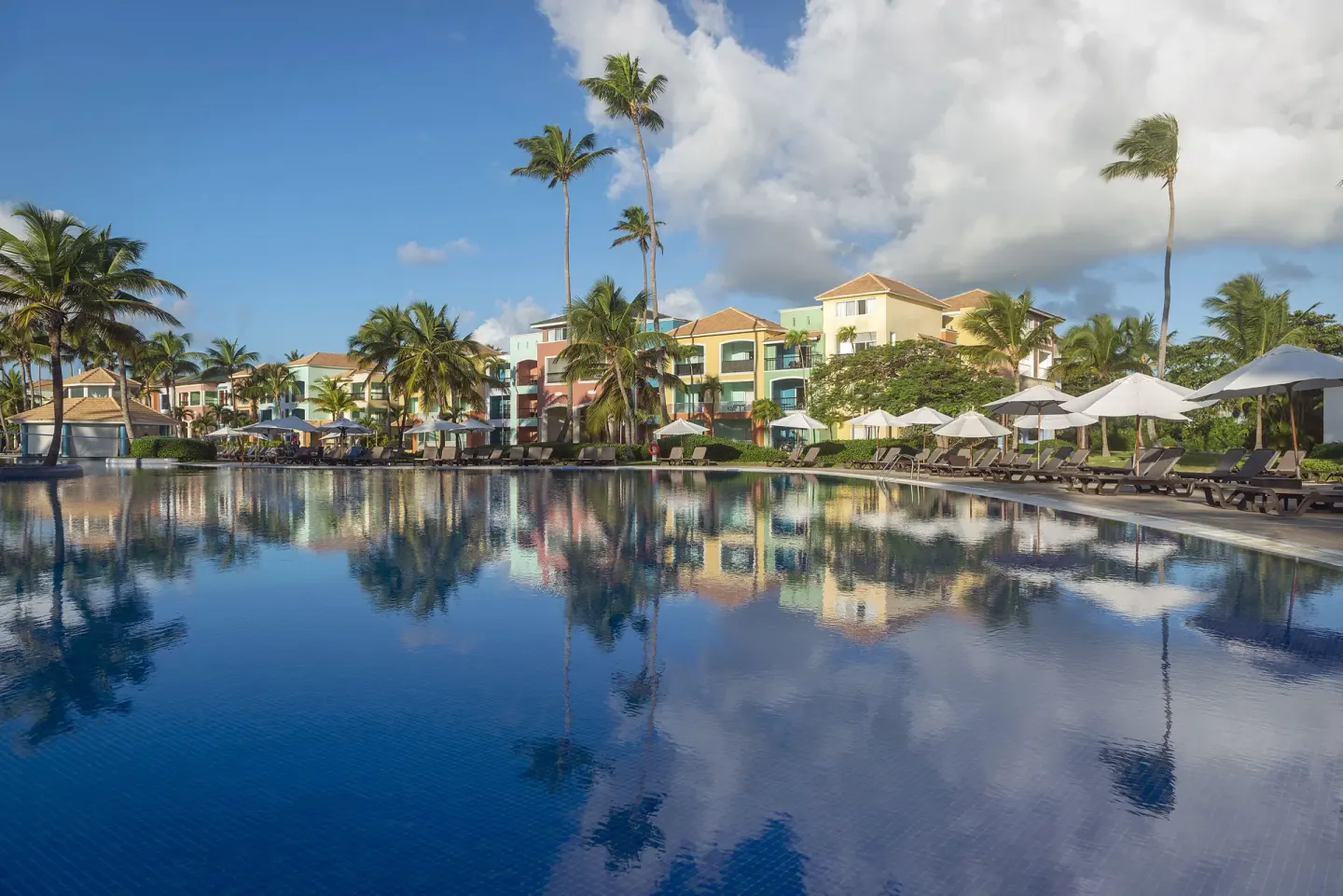 Poolside buildings, palms, loungers and umbrellas reflected at Ocean Blue & Sand Beach Resort.
