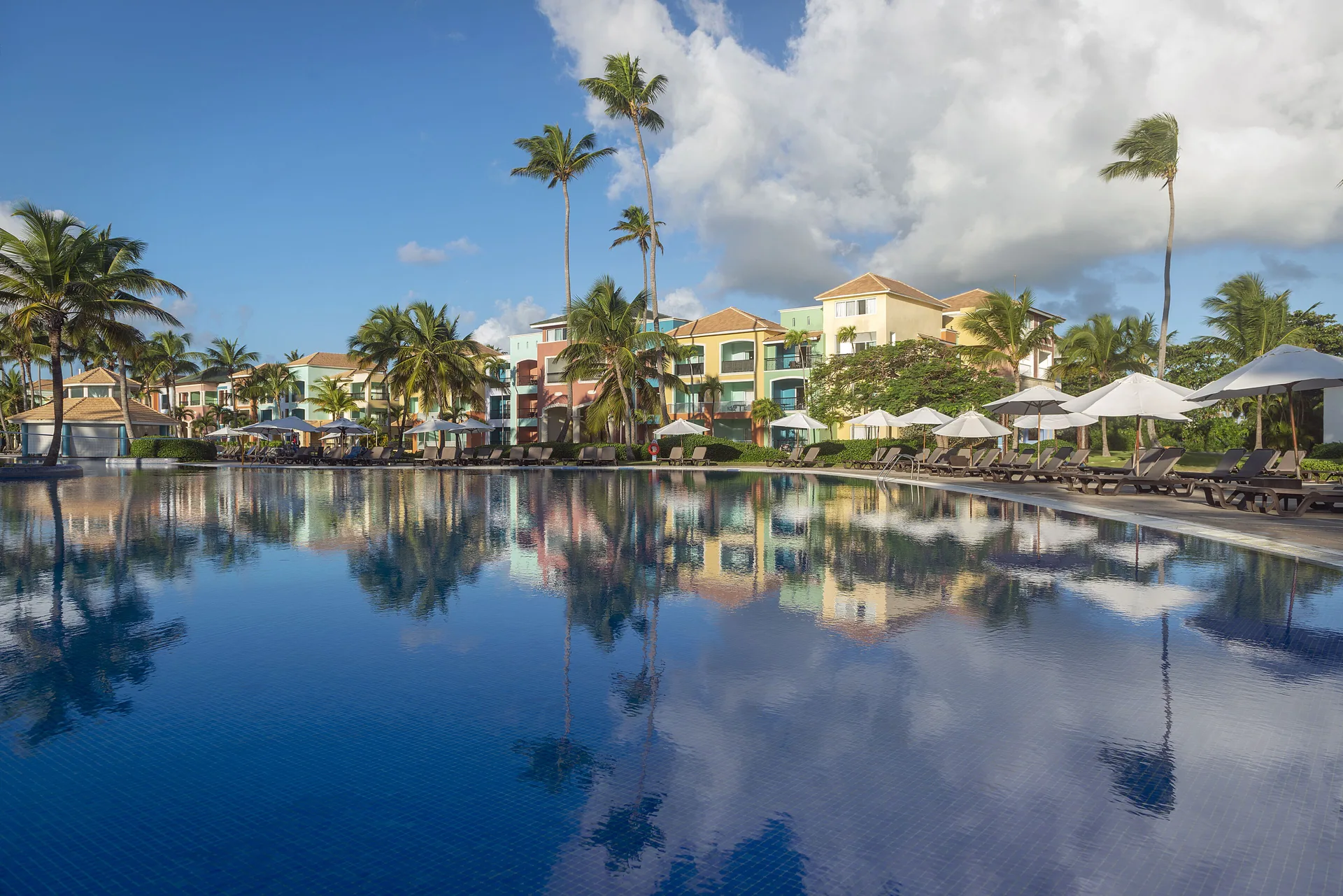 Poolside buildings, palms, loungers and umbrellas reflected at Ocean Blue & Sand Beach Resort.