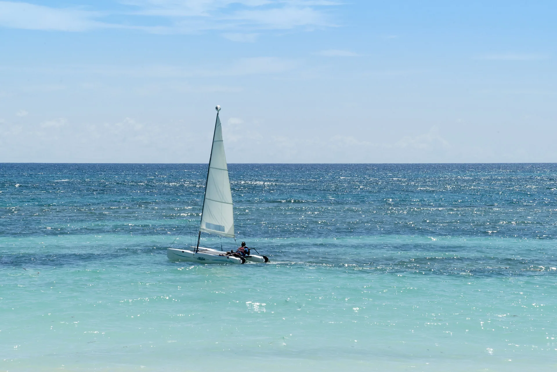 Small sailboat on turquoise water near Ocean Blue & Sand Beach Resort.