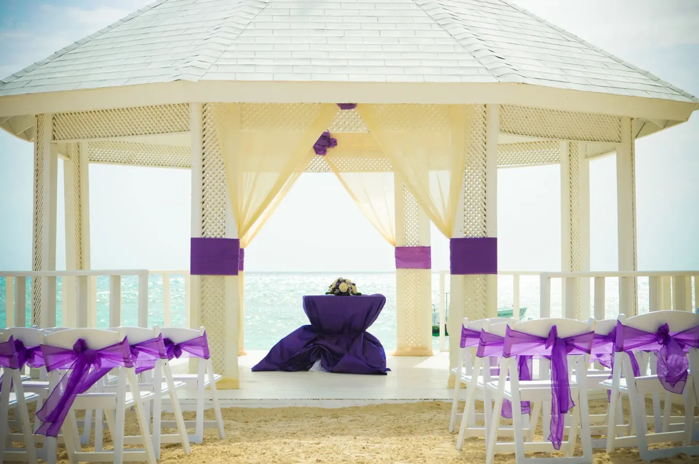 Beach wedding gazebo with white chairs and purple accents at Ocean Blue & Sand Beach Resort.
