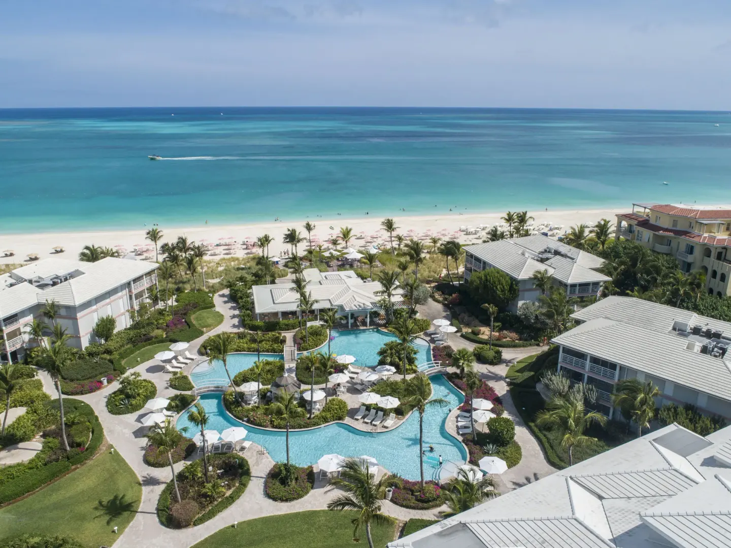 Aerial view of pools, gardens, resort buildings, and beach at Ocean Club West, Grace Bay Beach.