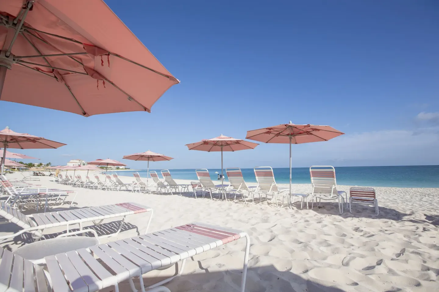 Beach chairs and pink umbrellas on the sand at Ocean Club West, Grace Bay Beach.