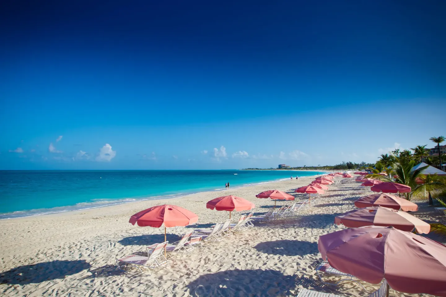 Pink umbrellas and lounge chairs on the beach at Ocean Club West, Grace Bay Beach.