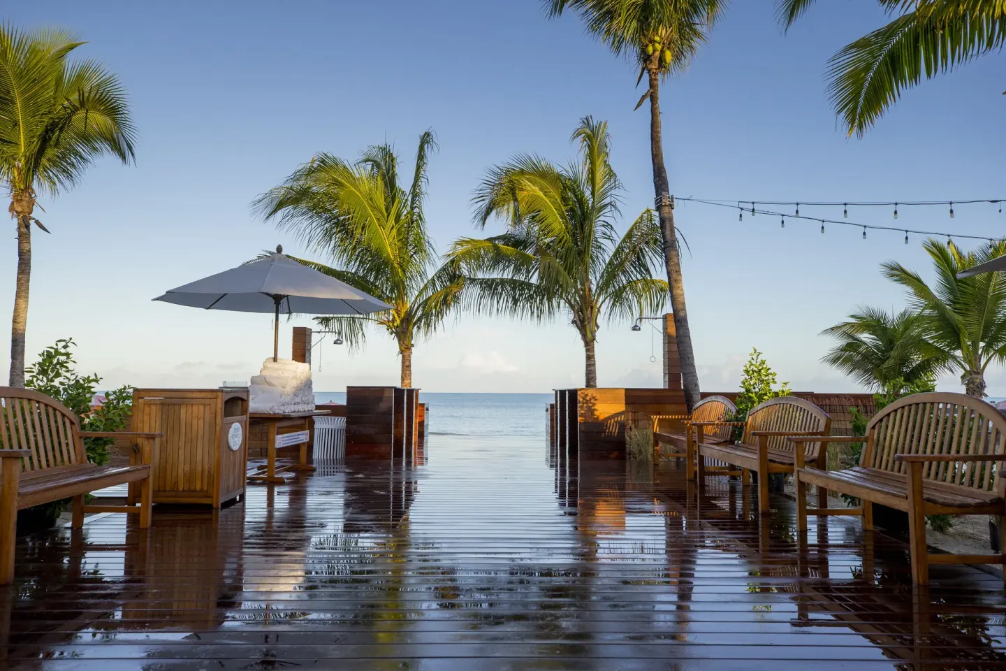 Wet wooden beach deck with benches and palms at Ocean Club West, Grace Bay Beach.