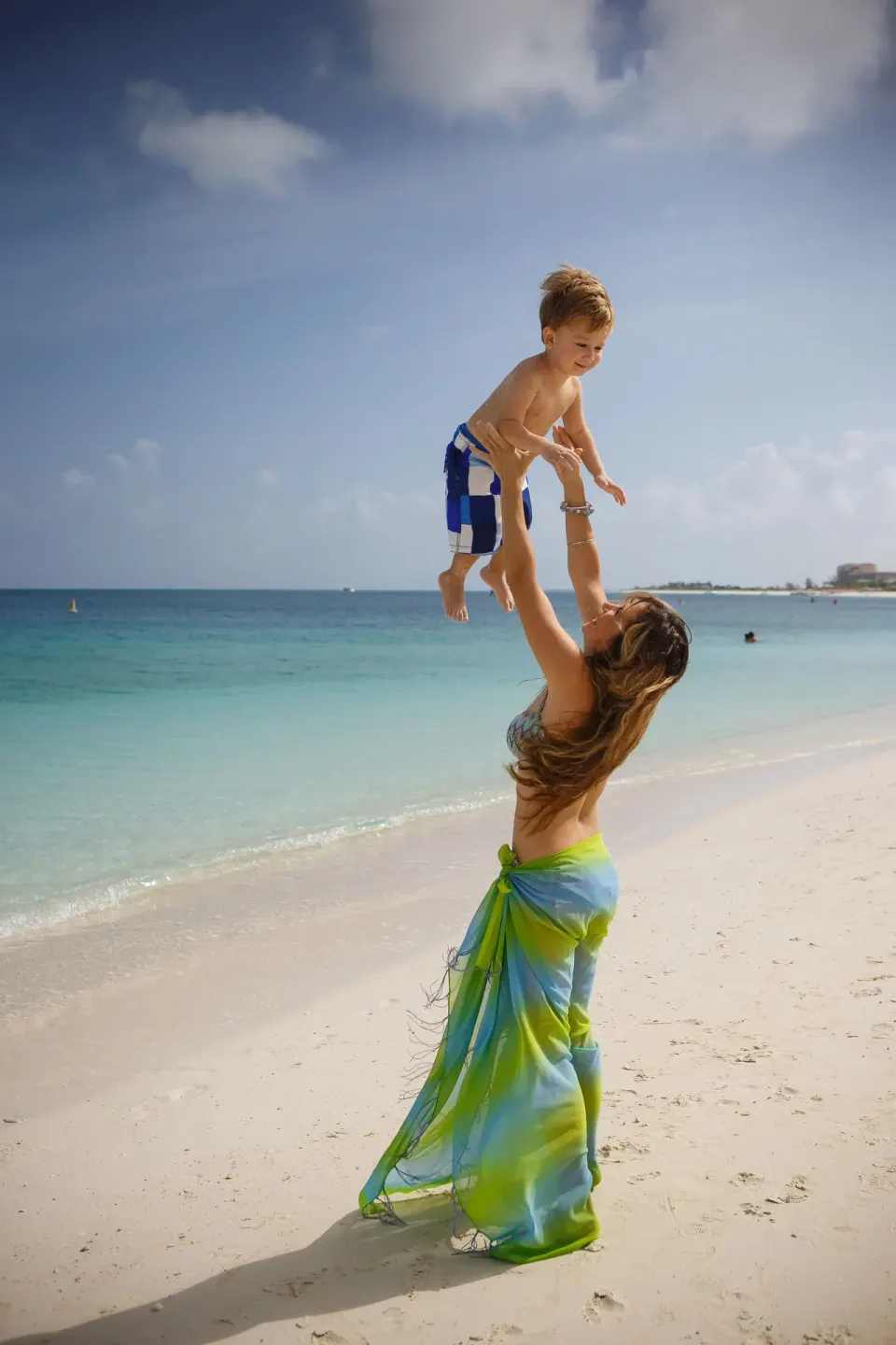 A woman lifts a child on the beach at Ocean Club West, Grace Bay Beach.