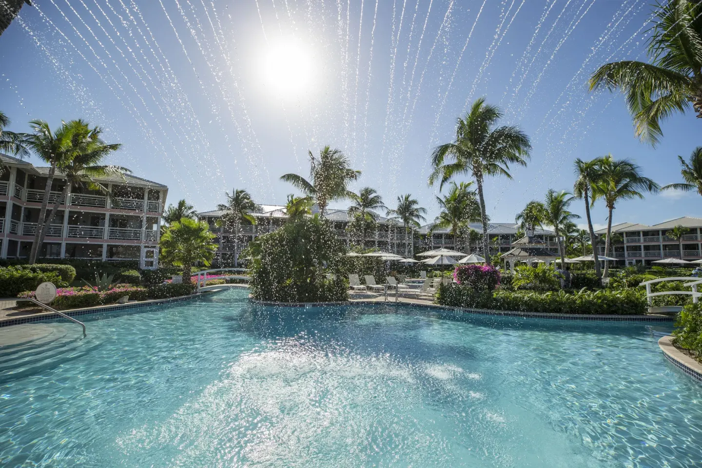 Pool fountain spraying water under palms and bright sun at Ocean Club West, Grace Bay Beach.