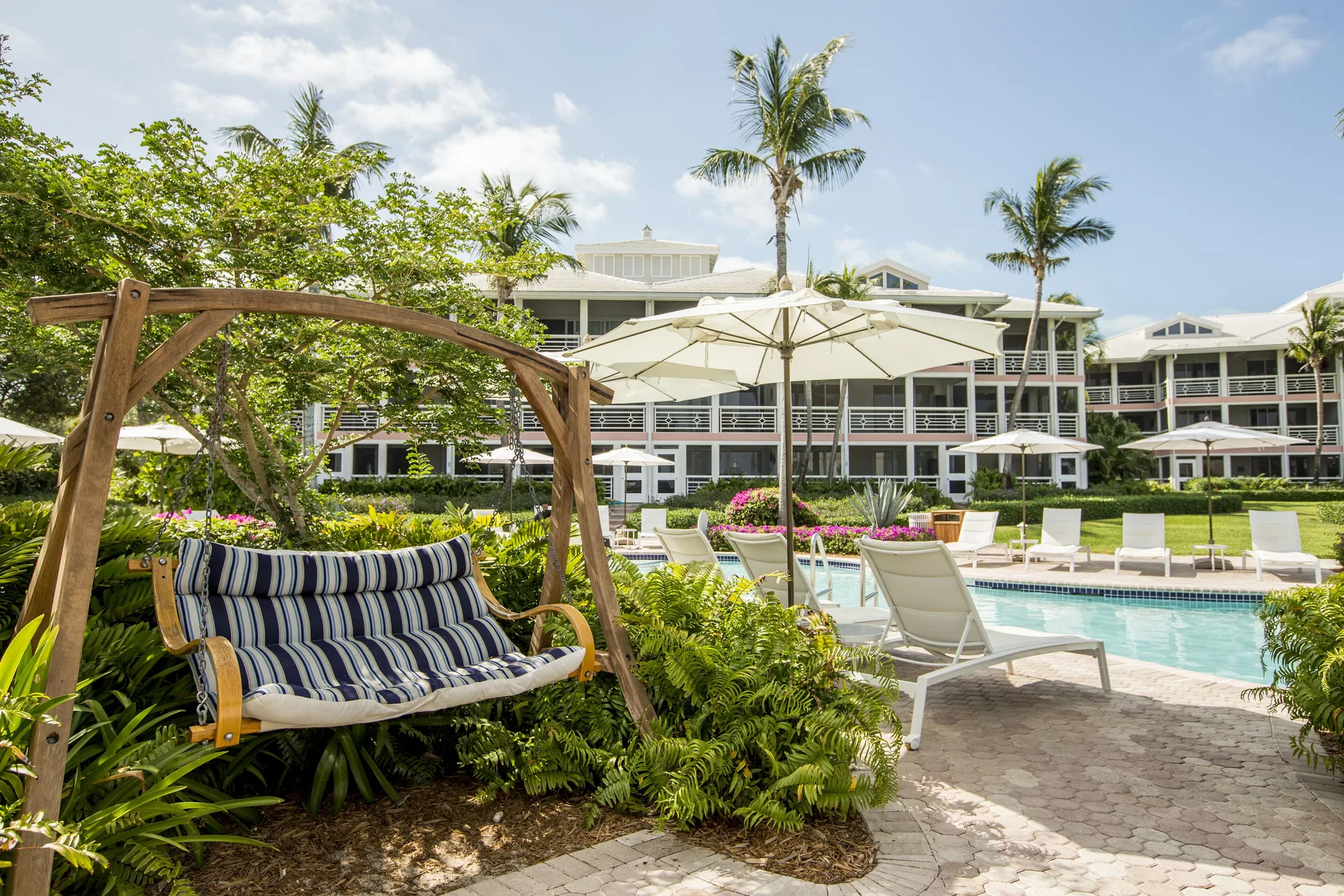 Poolside swing, loungers, umbrellas, and resort buildings at Ocean Club West, Grace Bay Beach.
