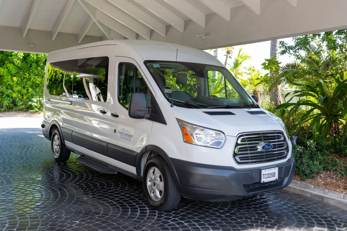 A white resort shuttle van is parked under the covered entrance at Ocean Club West, Grace Bay Beach.