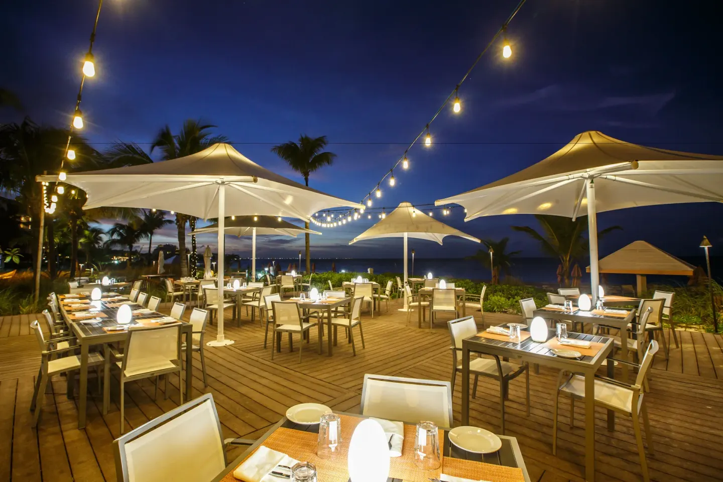 Beachfront dinner tables under umbrellas and string lights at Ocean Club West, Grace Bay Beach.