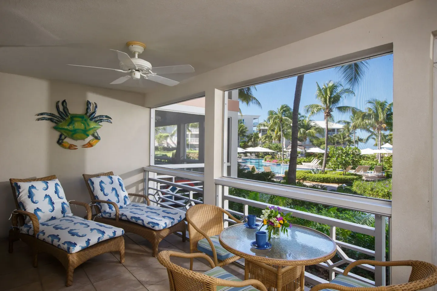 Balcony seating in a deluxe one-bedroom suite overlooking palms and pool at Ocean Club West, Grace Bay Beach.