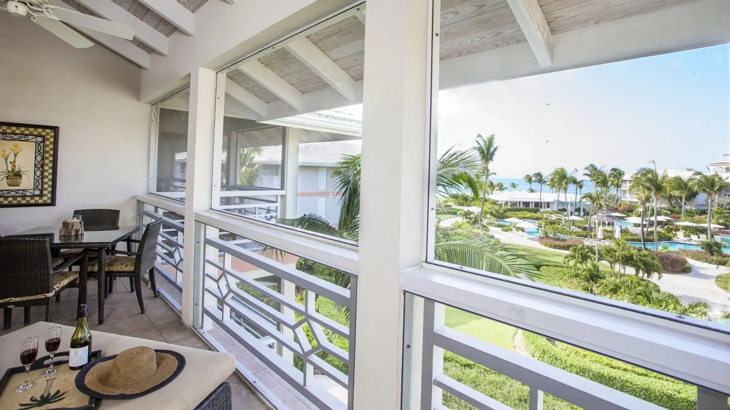Junior Suite balcony at Ocean Club West, Grace Bay Beach with dining table, wine glasses and partial ocean view.