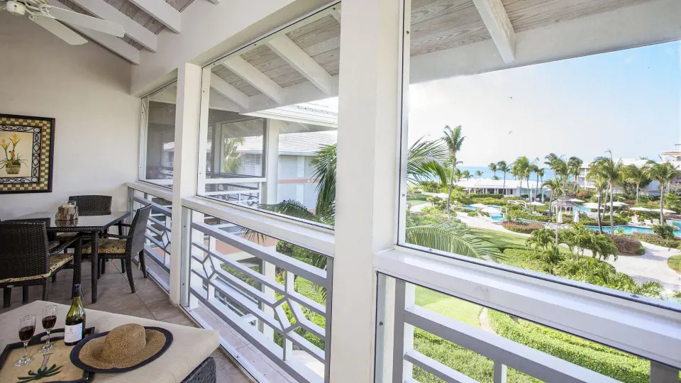 Junior Suite balcony at Ocean Club West, Grace Bay Beach with dining table, wine glasses and partial ocean view.