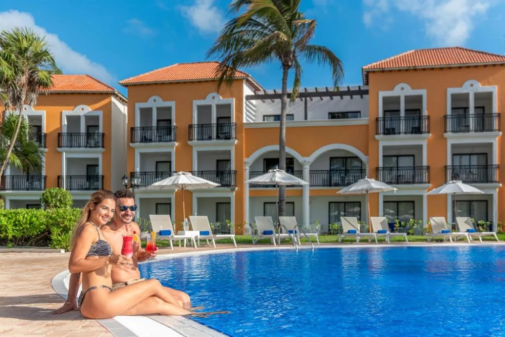 Couple with drinks beside a pool and guest buildings at Ocean Coral and Turquesa.