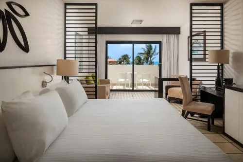 Junior Suite Ocean Coral and Turquesa room with white bedding and balcony seating at Ocean Coral and Turquesa.