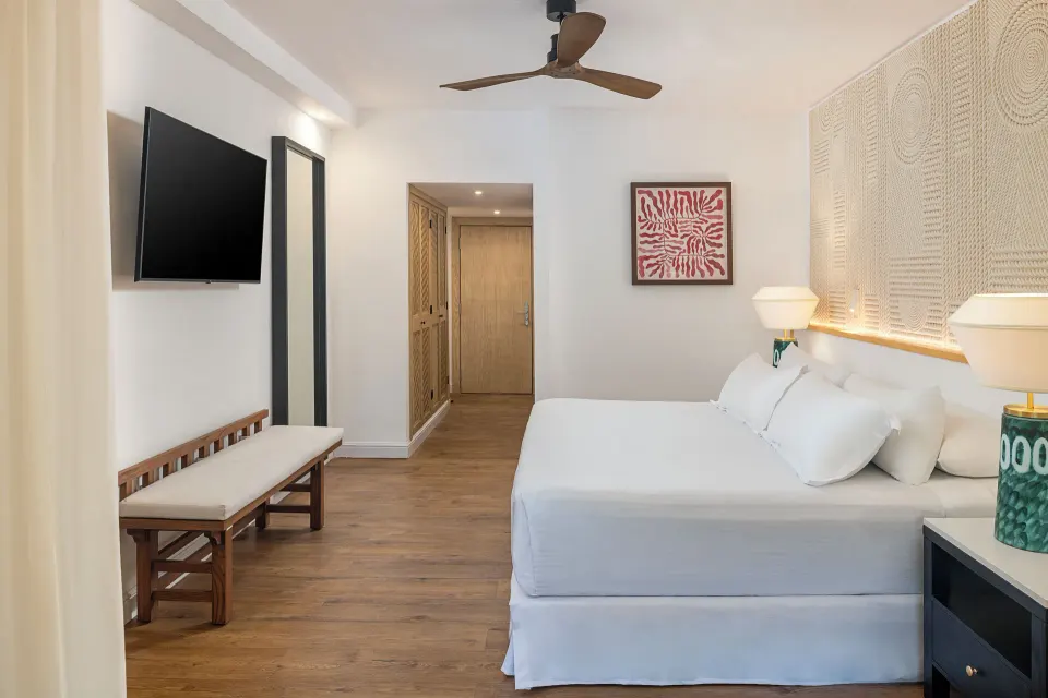 Junior Suite Waterpark Side king bed, bench, TV, and entry at Ocean Coral and Turquesa.