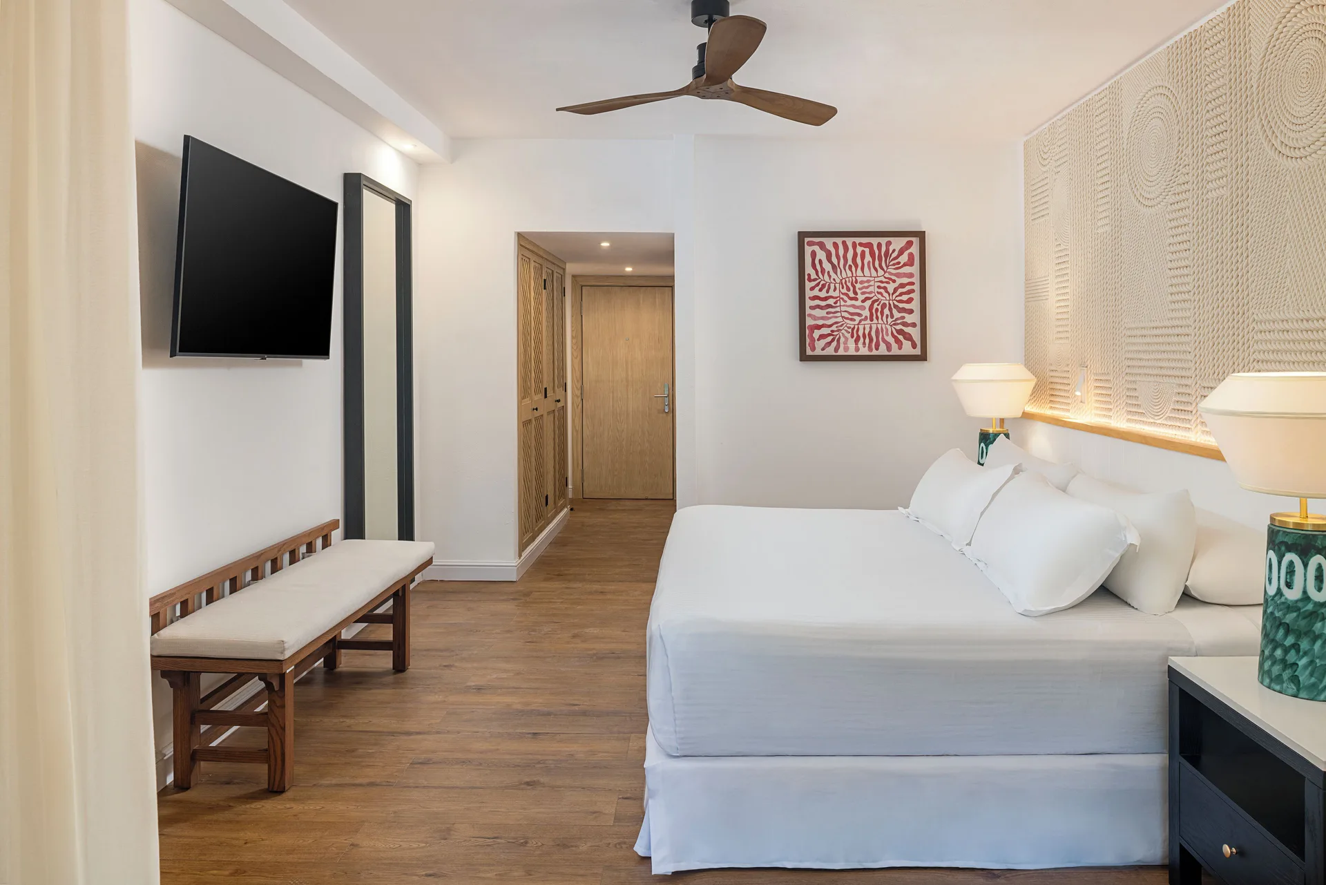 Junior Suite Waterpark Side king bed, bench, TV, and entry at Ocean Coral and Turquesa.