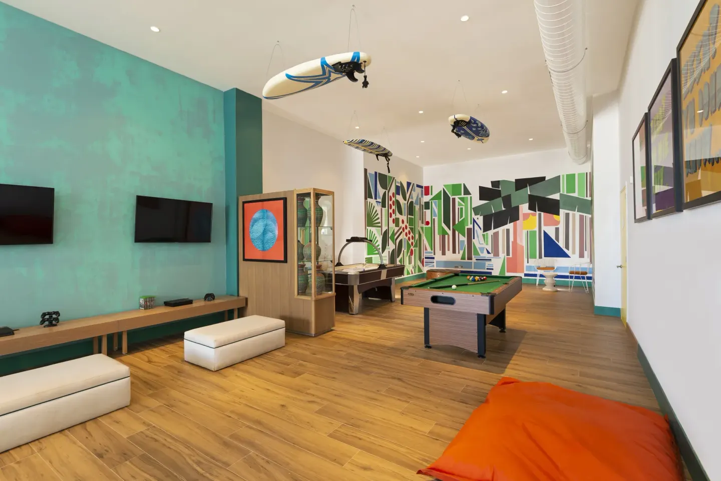 Game room with pool table, wall-mounted TVs, and surfboard decor at Ocean Coral Spring.