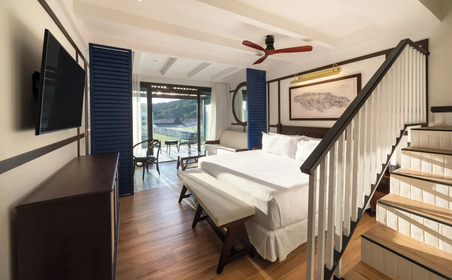 Guest room with white king bed, wall-mounted TV, stairs, and balcony doors at Ocean Coral Spring.