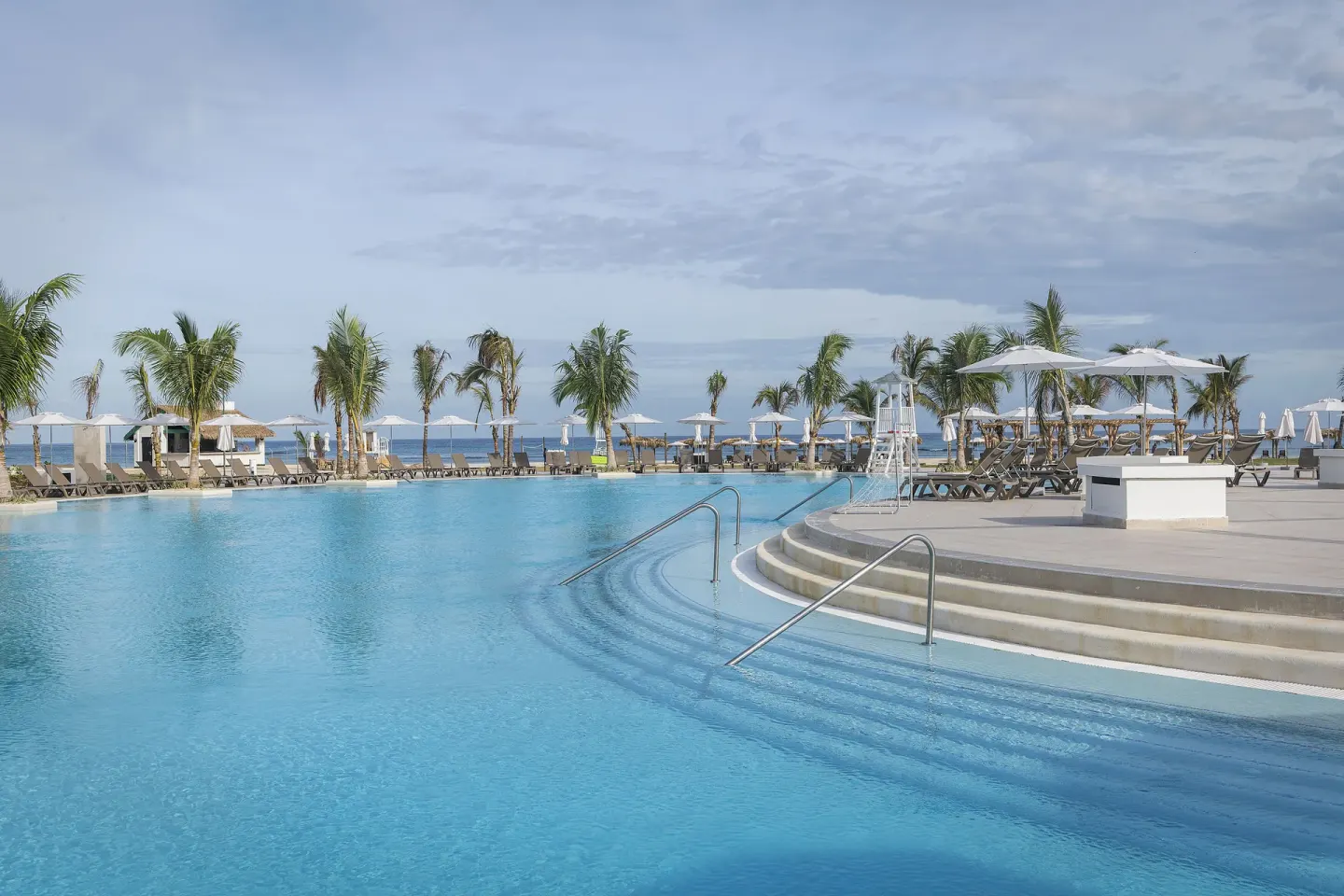 Large oceanfront pool with palm trees, loungers, and umbrellas at Ocean Coral Spring.