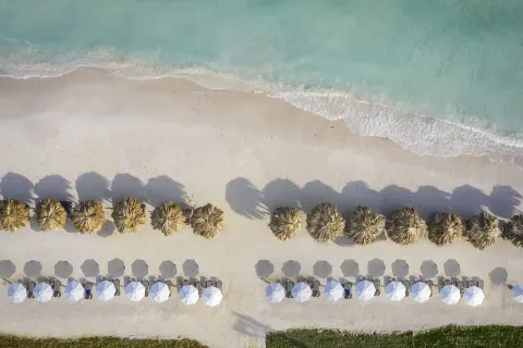 Overhead view of beach umbrellas, palapas, and turquoise water at Ocean Coral Spring.