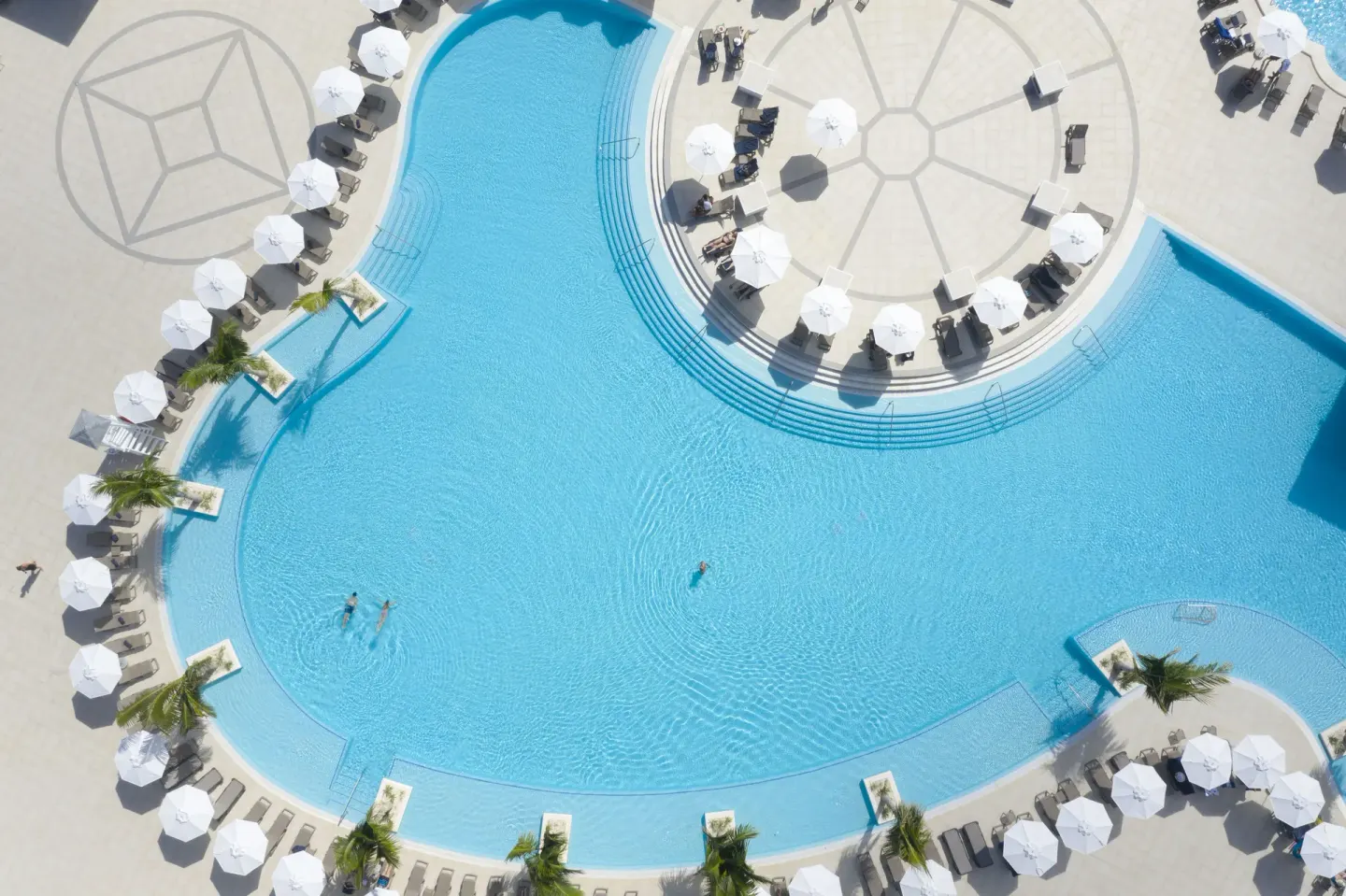 Top-down view of a large pool with umbrellas and loungers at Ocean Coral Spring.