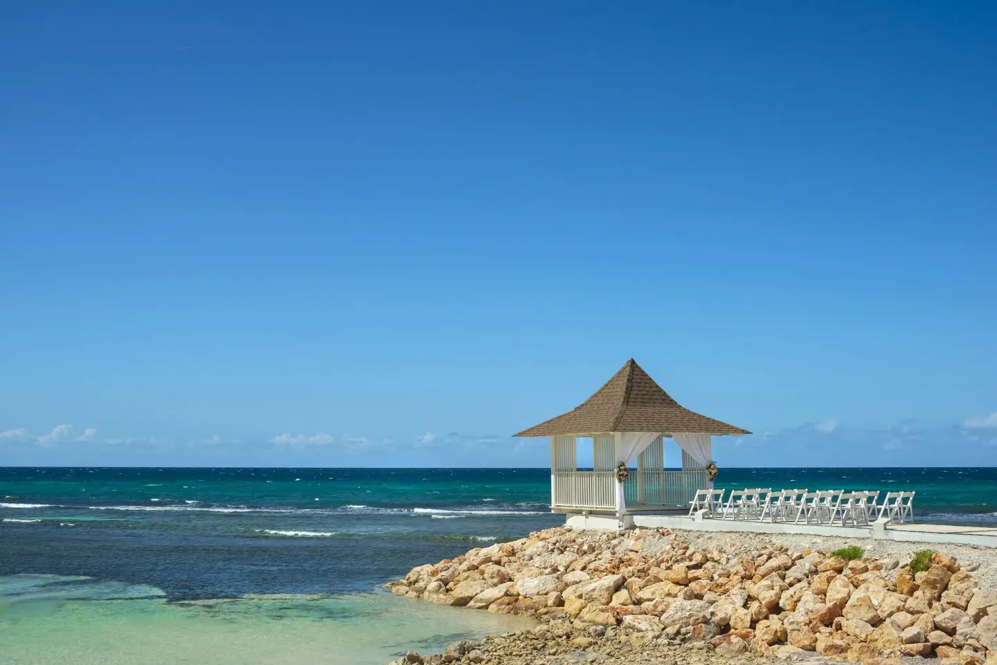 Seaside wedding gazebo and white chairs on a rocky point at Ocean Coral Spring.