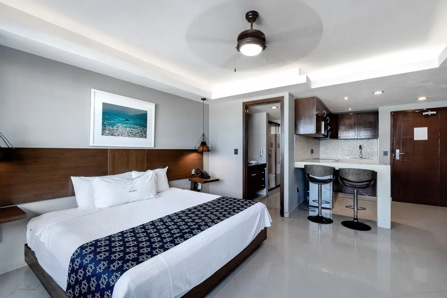 Guest room with king bed, kitchenette, bar stools, and open bathroom door at Ocean Dream Cancun.
