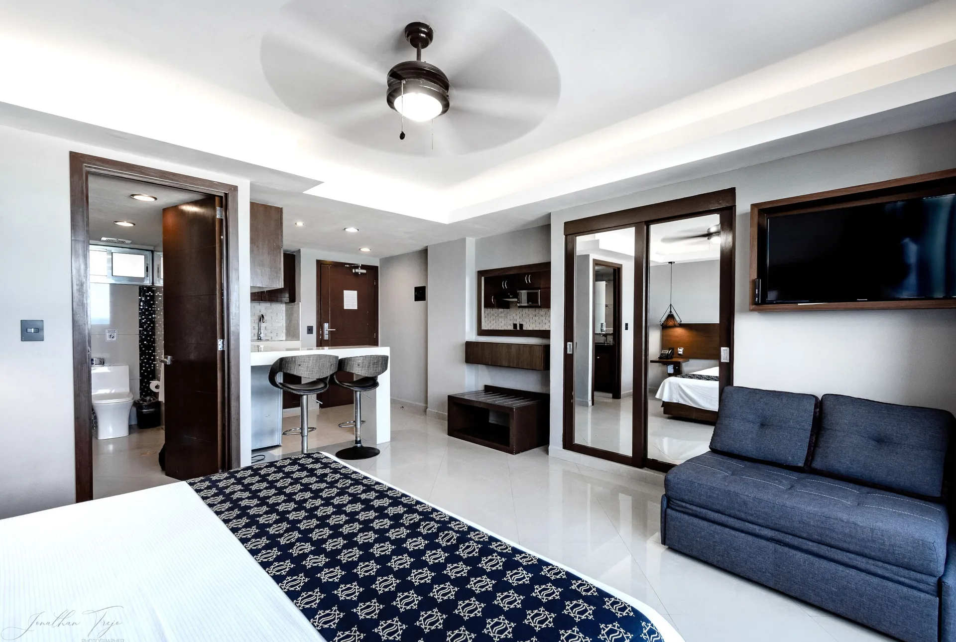 Guest room with king bed, blue sofa, kitchenette, bathroom, and wall TV at Ocean Dream Cancun.