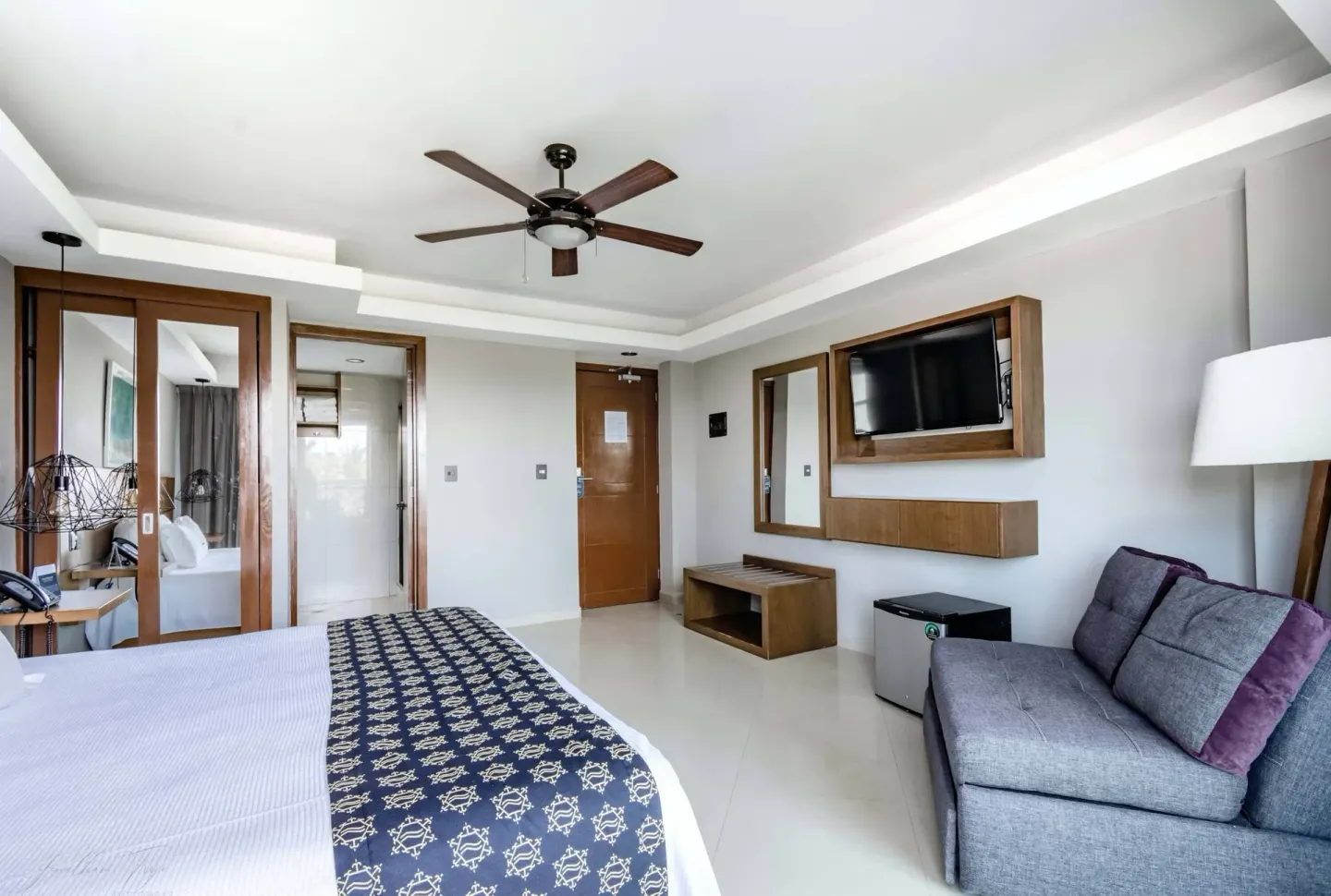 Guest room with king bed, sofa, wall TV, and mini fridge at Ocean Dream Cancun.