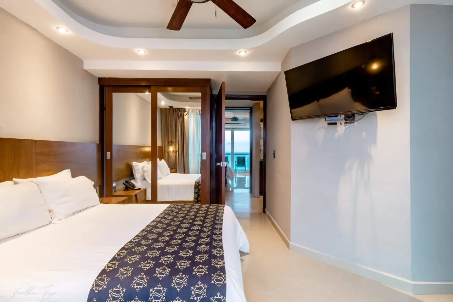 Guest room with king bed, wall TV, mirrored closet, and distant ocean view at Ocean Dream Cancun.