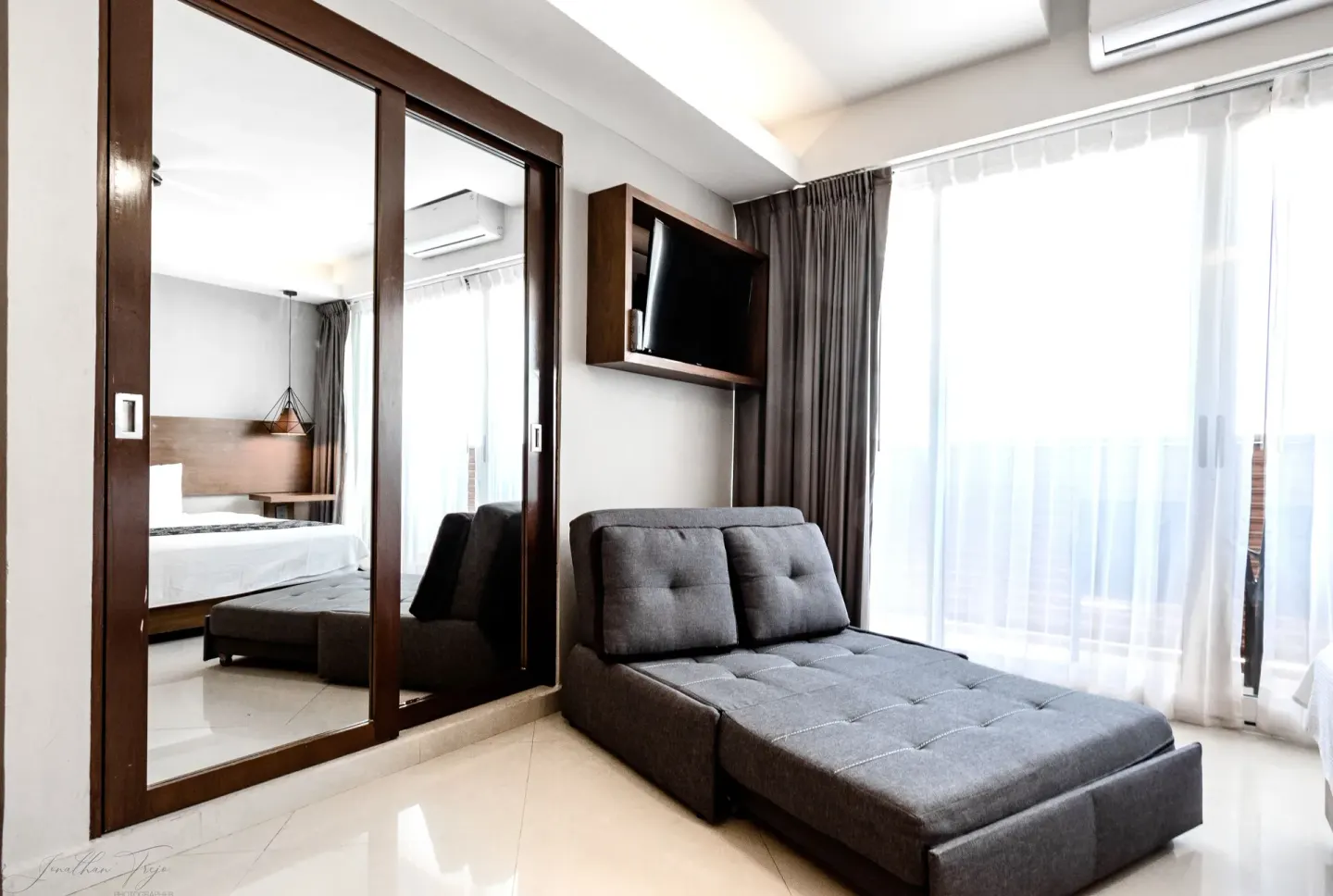 Guest room sitting area with gray chaise sofa, mirrored closet, and balcony curtains at Ocean Dream Cancun.