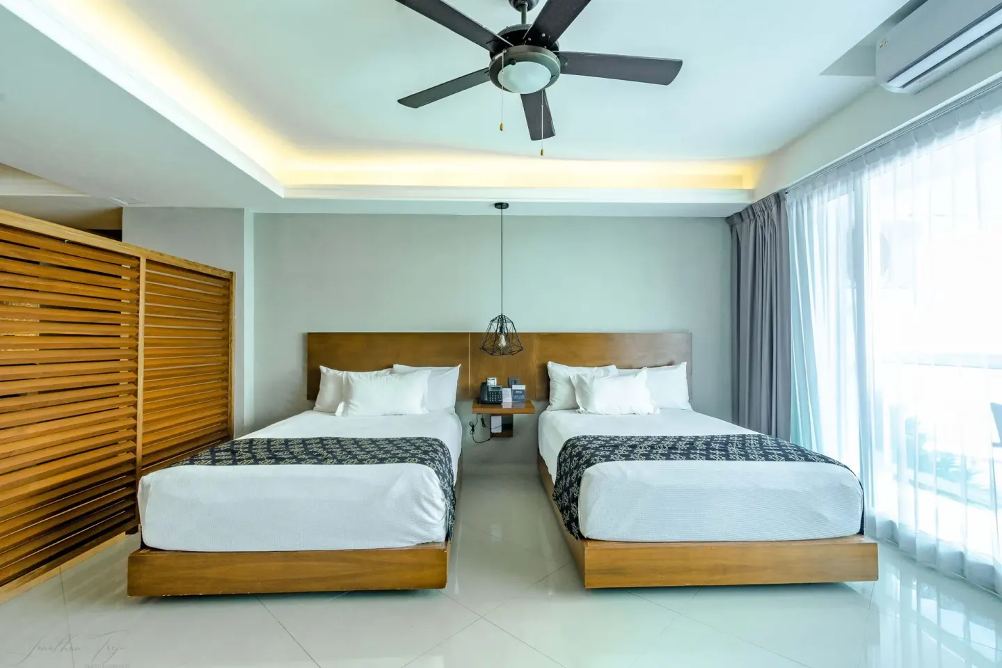 Guest room with two beds, wood privacy screen, and sheer curtains at Ocean Dream Cancun.