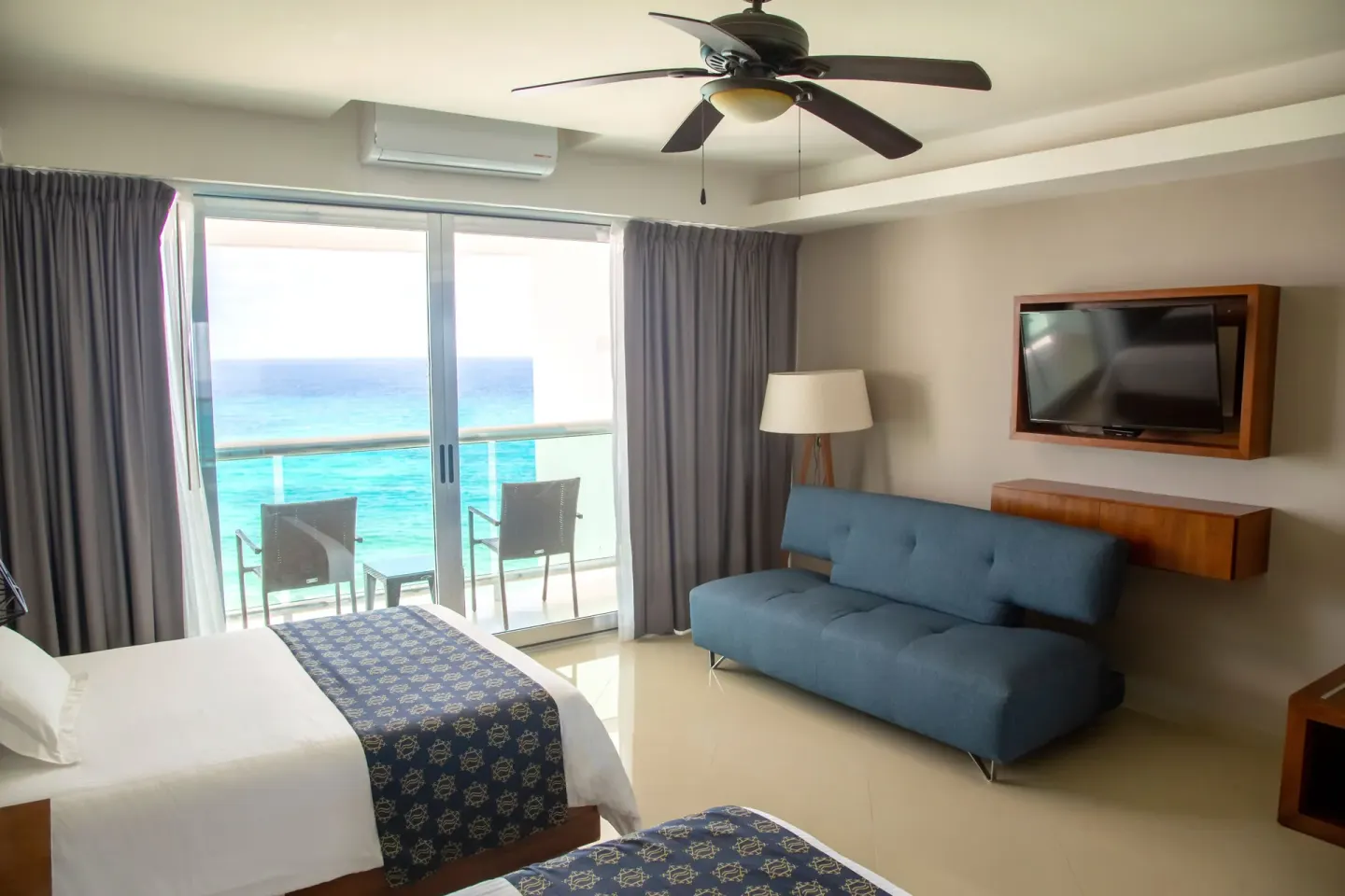 Guest room seating area with two beds, blue sofa, TV, and ocean balcony at Ocean Dream Cancun.