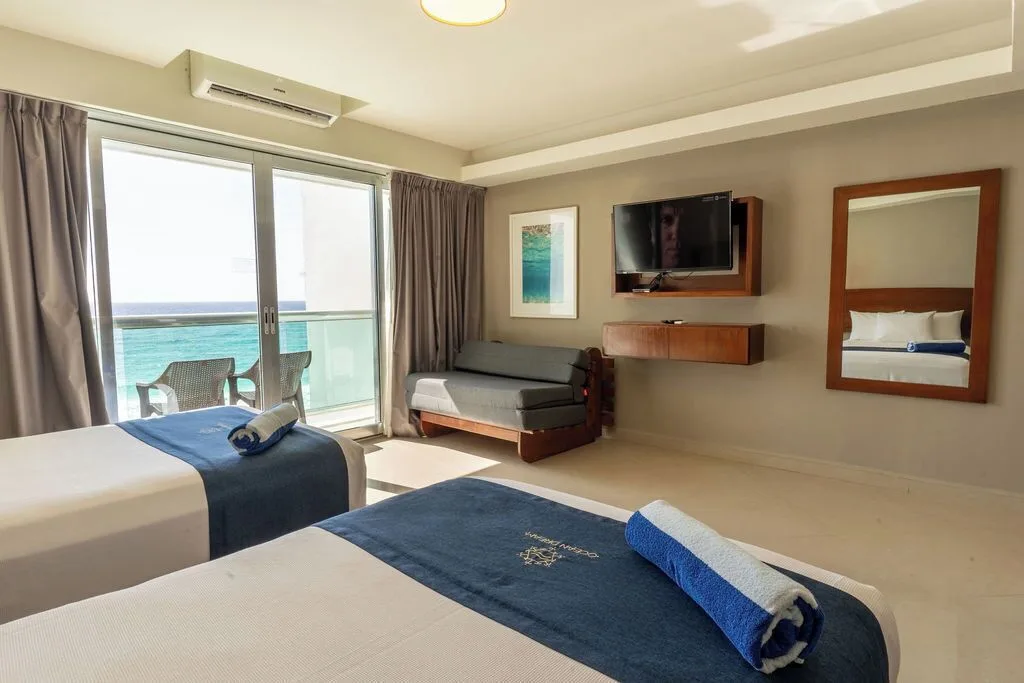 Deluxe room with two beds, sofa, TV, mirror, and ocean balcony at Ocean Dream Cancun.
