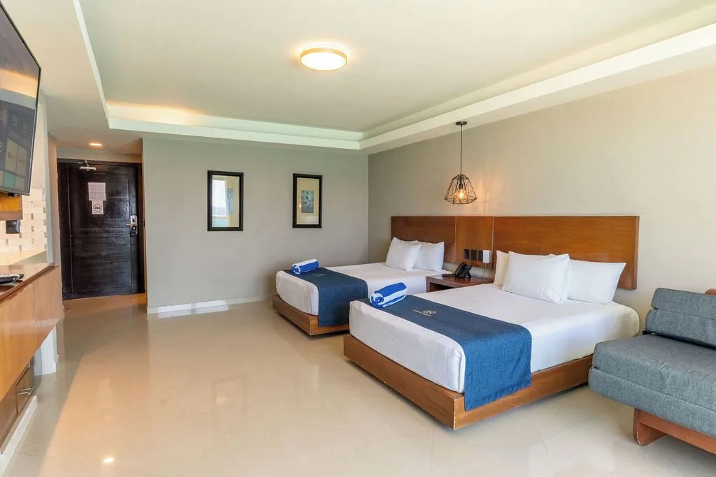 Deluxe room with two beds, sofa, TV, and entry door at Ocean Dream Cancun.