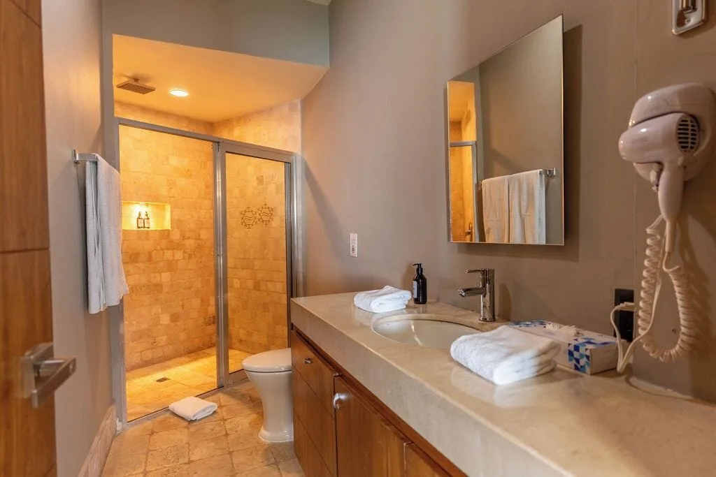 Diamond Suite bathroom with glass shower, vanity, towels and wall hair dryer at Ocean Dream Cancun.