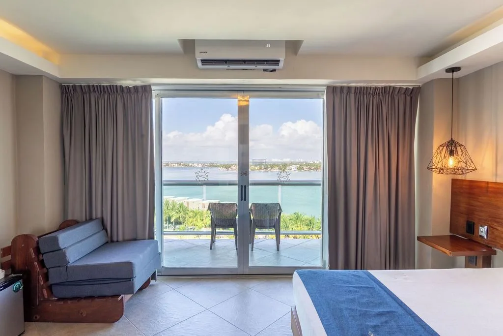 Standard Room lagoon view with bed, sofa and balcony at Ocean Dream Cancun.