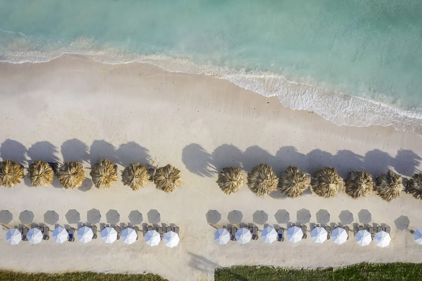 Aerial view of beach umbrellas, palapas, sand, and turquoise water at Ocean Eden Bay.