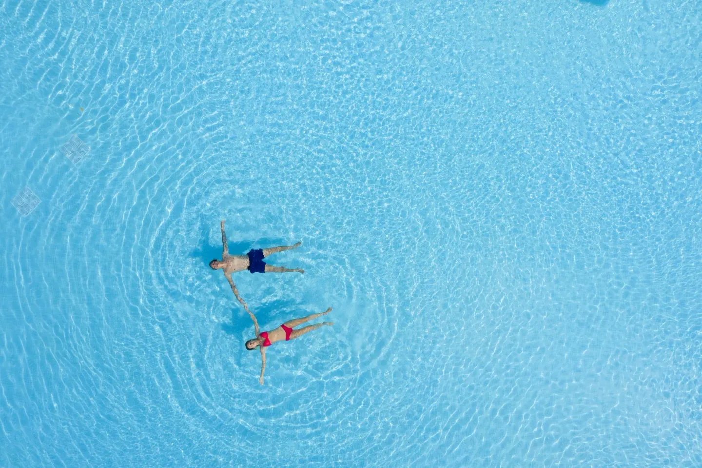 Two swimmers floating in bright blue pool water at Ocean Eden Bay.