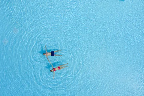 Two swimmers floating in bright blue pool water at Ocean Eden Bay.